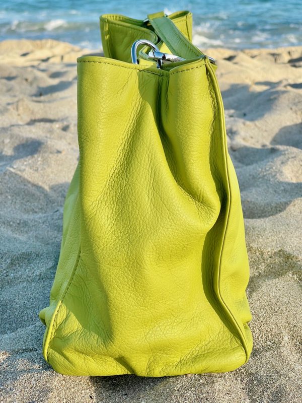 Tahitian lime leather bag side view on a sandy beach with ocean in the background