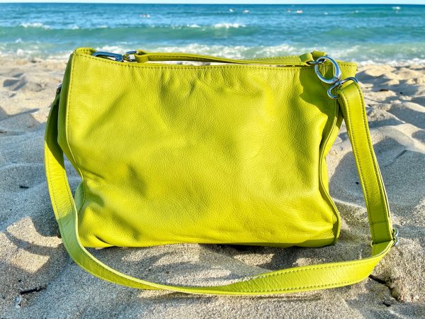 Front view of tahitian lime bag on beach sand, featuring both long crossbody strap and short shoulder strap