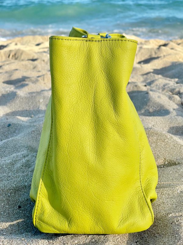 Tahitian lime leather bag side view on a sandy beach with ocean in the background