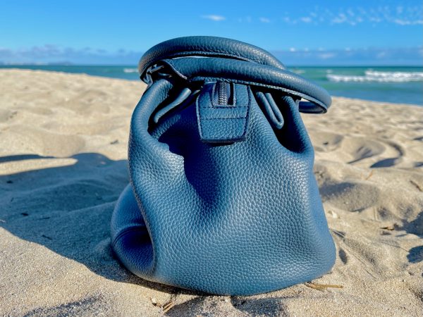 Denim Blue leather bag side view on a sandy beach with ocean in the background