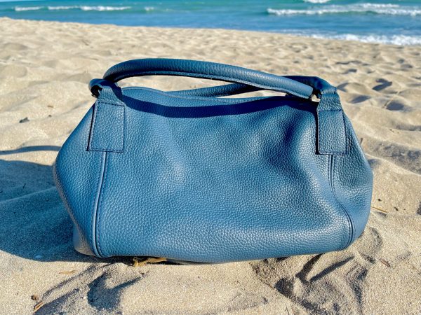 Denim Blue bag with slouchy structureon a sandy beach with ocean in the background