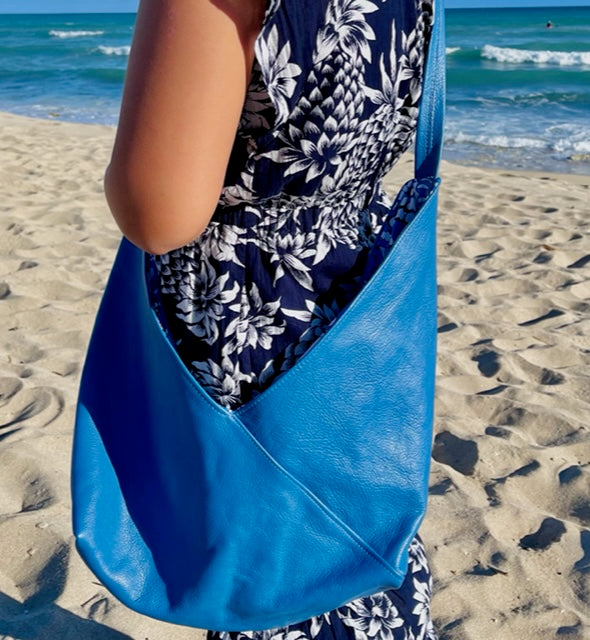A woman wearing a floral dress holding a Cobalt Blue leather hobo bag as a crossbody bag with untied long strap