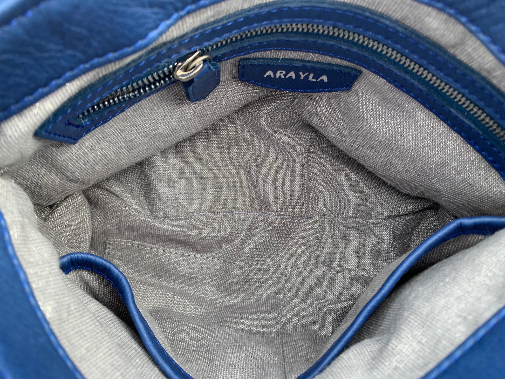 Silver grey metallic textile lining interior of a bag with blue zipper pocket and Arayla brand label.