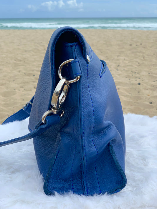 Blue Marine bag side view on a fluffy white surface with a beach in the background