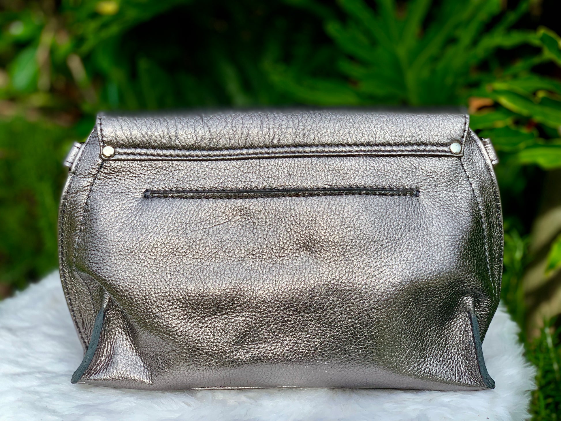Pewter Metallic bag back view on a white surface with green leaves in the background