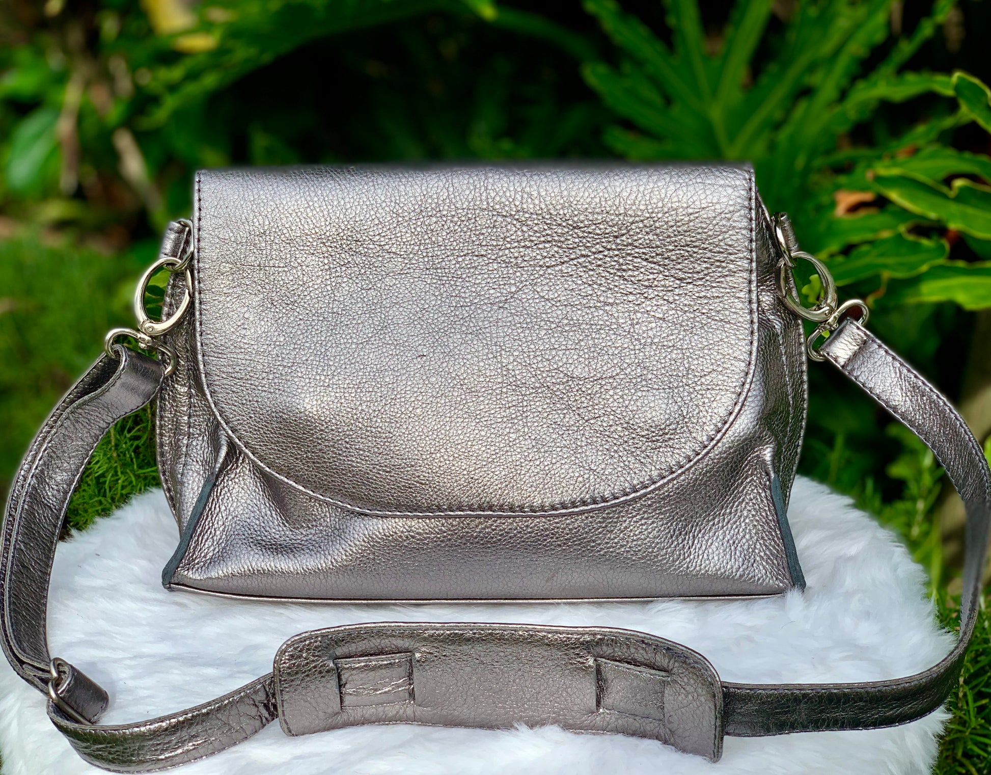 Pewter Metallic leather bag front view, on a white surface with green foliage in the background