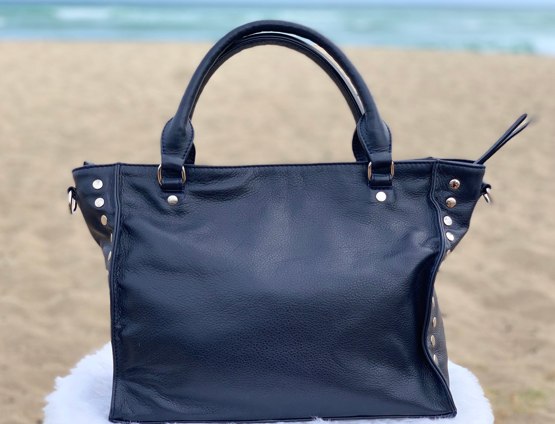 Sapphire leather satchel bag back view on a sandy beach with ocean in the background