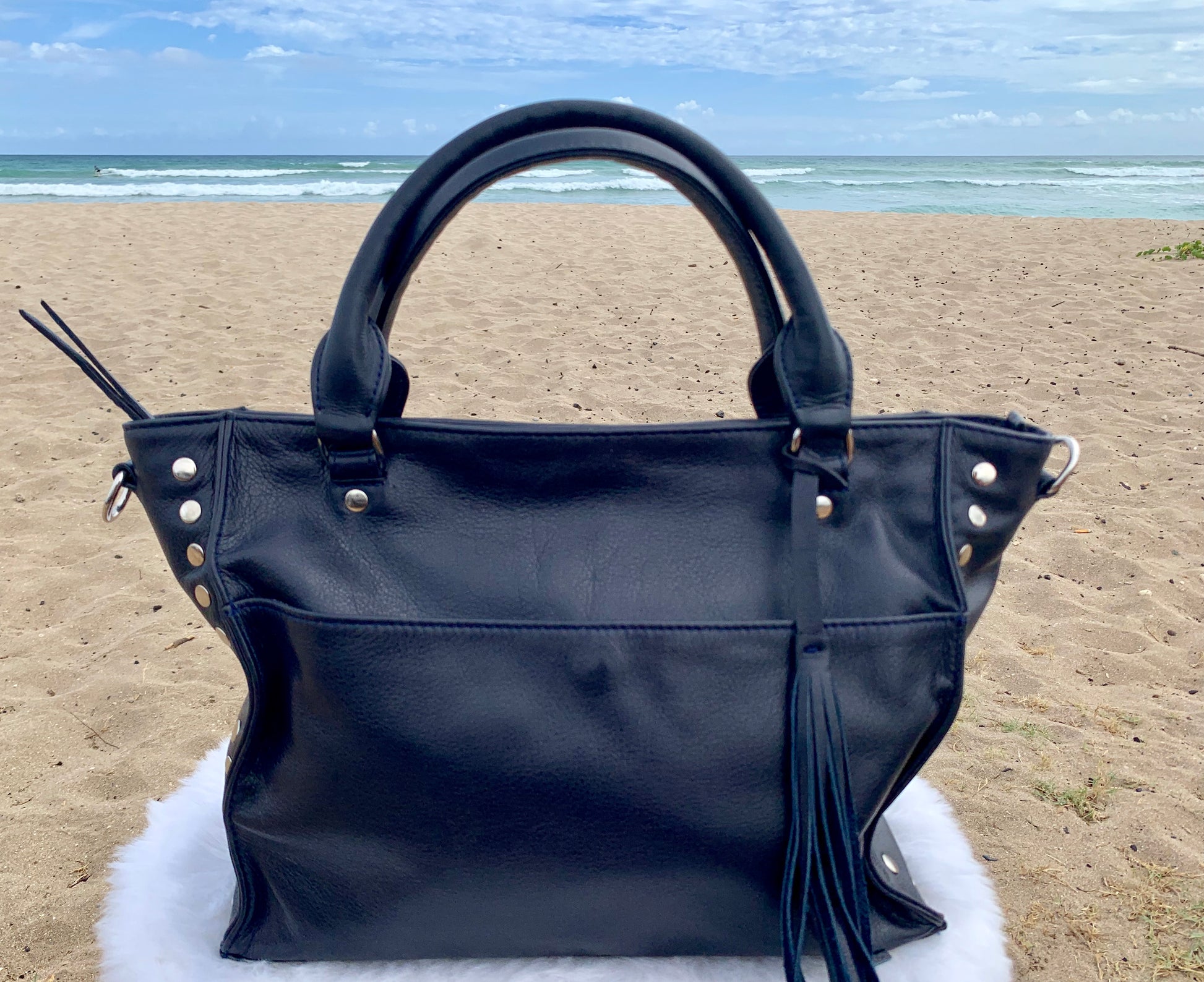 Sapphire leather satchel bag with tassels on a fluffy white surface with a beach background