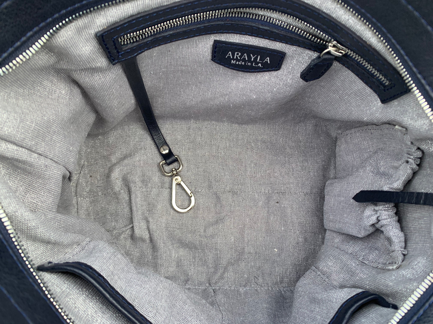 Close-up of the sapphire leather satchel bag interior with silver grey shimmer textile lining, key leash, zip pocket, two slip mobile pockets and sunglasses pocket.