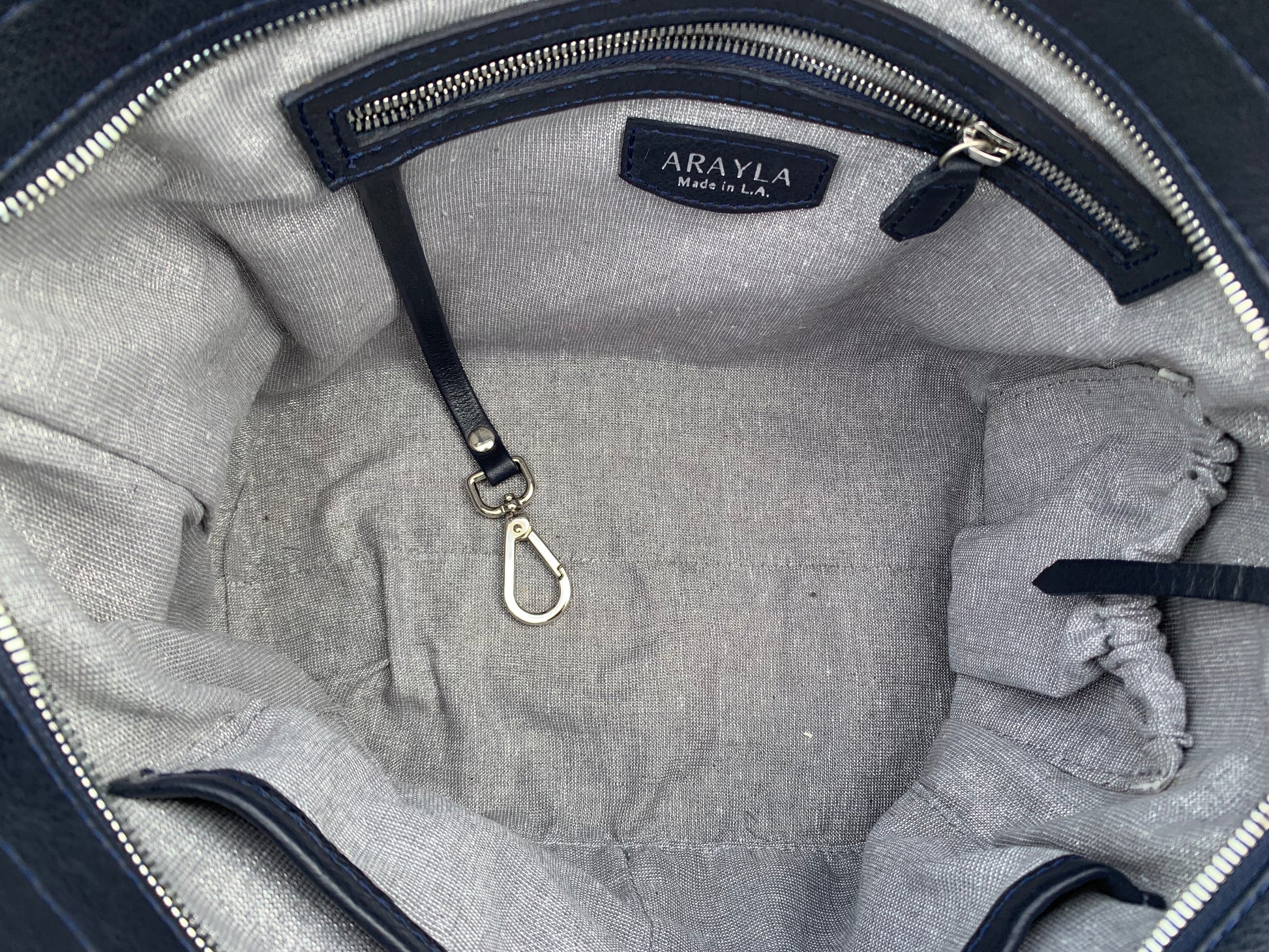 Close-up of the sapphire leather satchel bag interior with silver grey shimmer textile lining, key leash, zip pocket, two slip mobile pockets and sunglasses pocket.