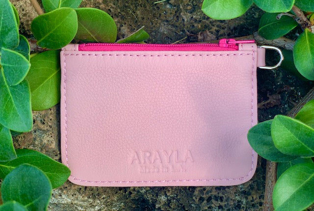 Light Pink pouch front view with a bright pink zipper on a stone surface surrounded by green leaves
