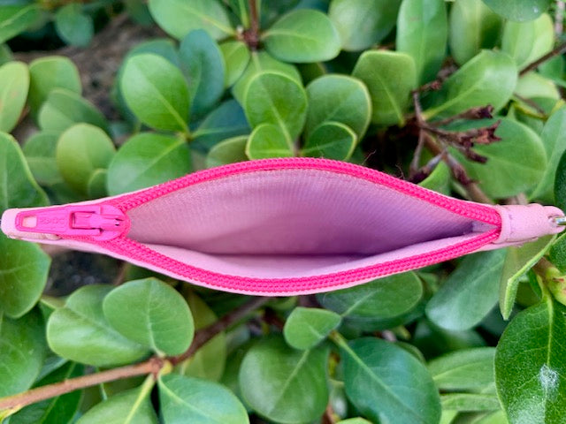 Close-up on the interior of the opened Light Pink pouch with a bright pink zipper surrounded by green leaves