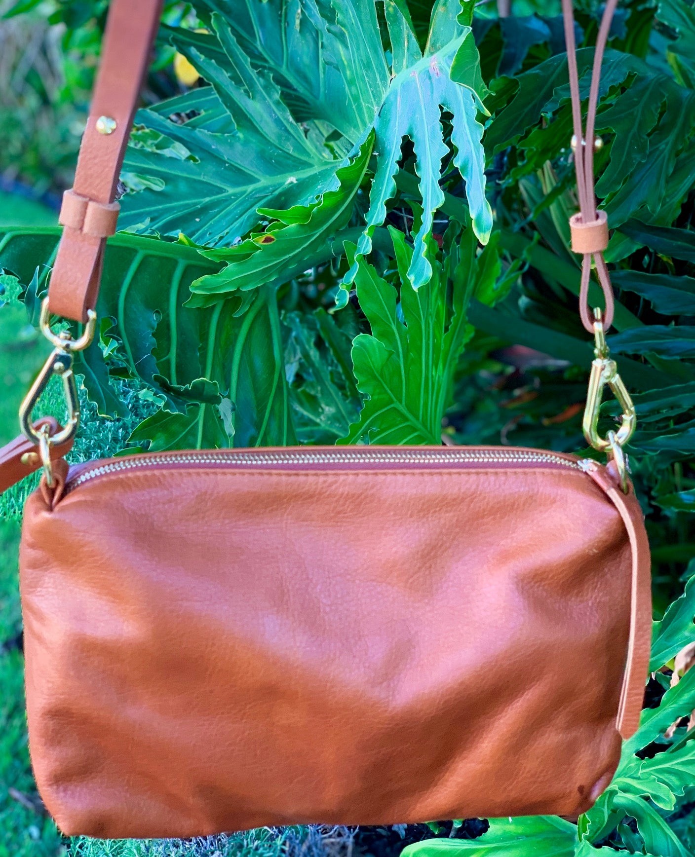 Whisky brown butter leather bag back view with a strap against a green leafy background