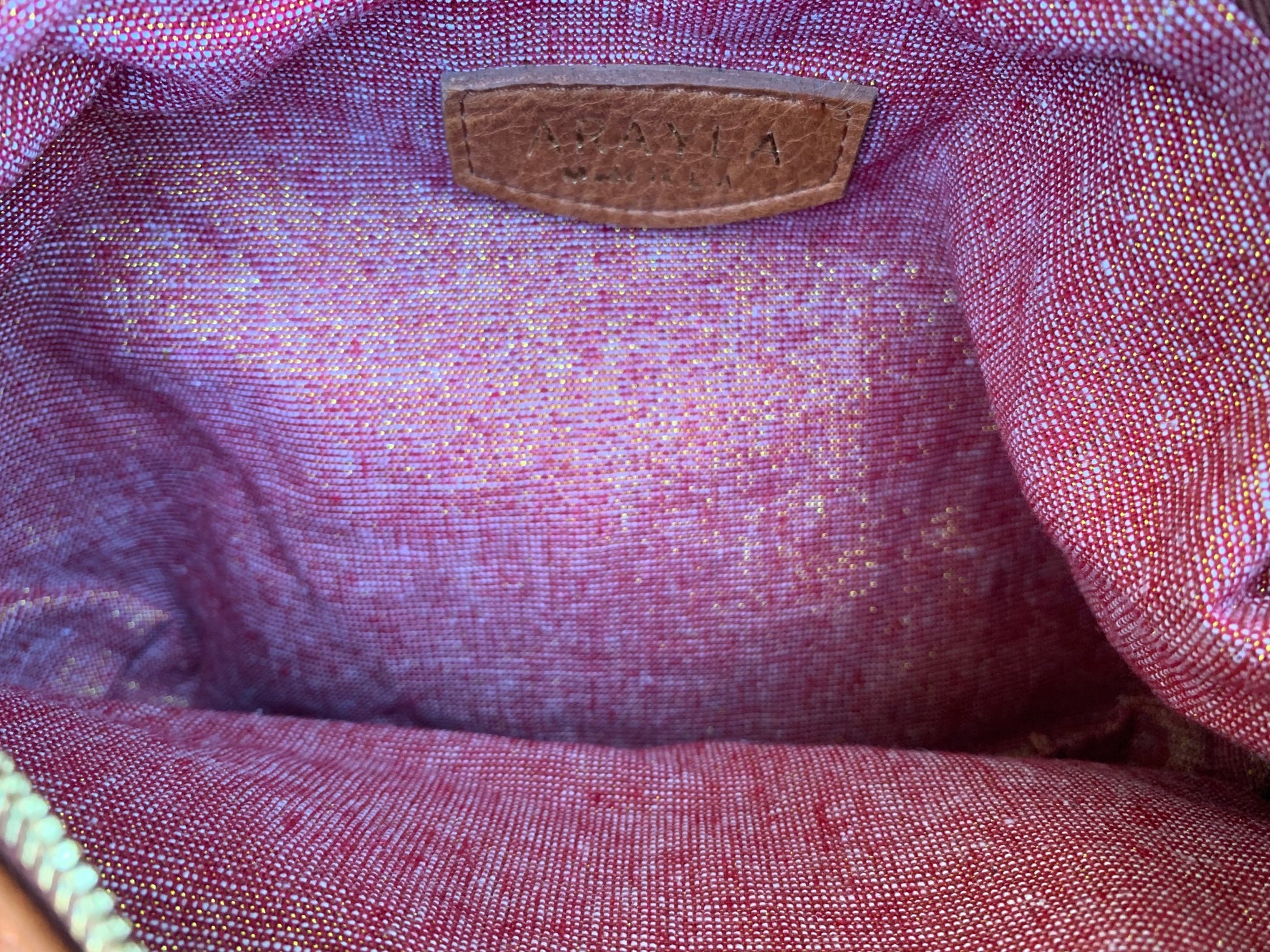 Close-up of theplum purple sheen leather interior with a visible brand logo on a red golden metallic textile lining.