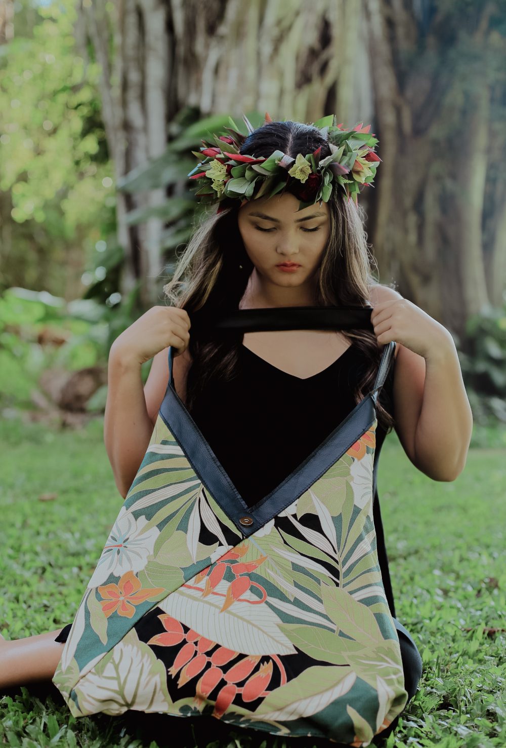 A woman wearing a black dress holding the Black Lava leather bag reversed to show the Hawaiian barkcloth lining.