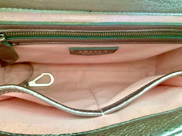 Close-up of the pewter metallic bag  interior with a visible brand logo on a pale pink with iridescent shimmer textile lining, key leash, zip pocket, and two slip mobile pockets.