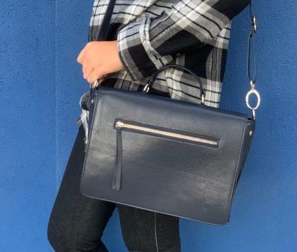 A woman holding a sapphire leather bag on her shoulder against a blue background