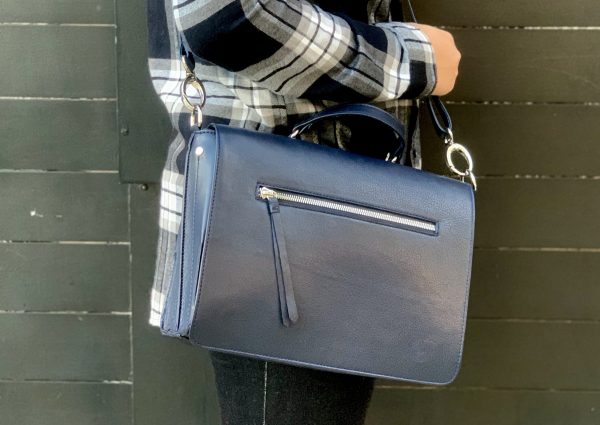 A woman holding a shappire leather bag on her shoulder against a dark background