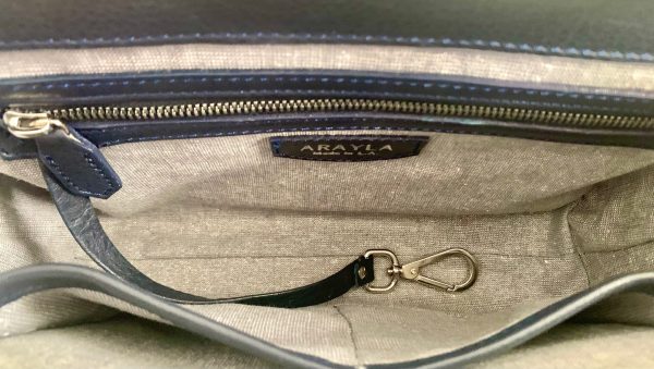 Close-up of the whisky brown leather bag  interior with a visible brand logo on a Silver grey metallic textile lining, key leash, zip pocket, and two slip mobile pockets.