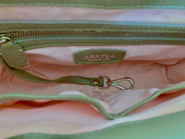 Close-up of the warm grey silky leather bag interior with a visible brand logo on a Pale pink with iridescent shimmer textile lining, key leash, zip pocket, and two slip mobile pockets.