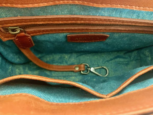 Close-up of the whisky brown leather bag  interior with a visible brand logo on a golden green metallic textile lining, key leash, zip pocket, and two slip mobile pockets.