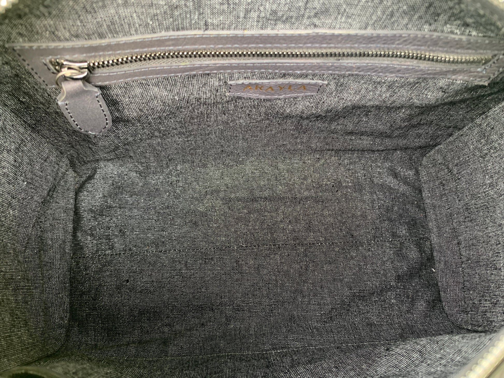Close-up of the titanium gray leather bag  interior with a visible brand logo on a Silver black textile lining, zip pocket, and two slip mobile pockets.