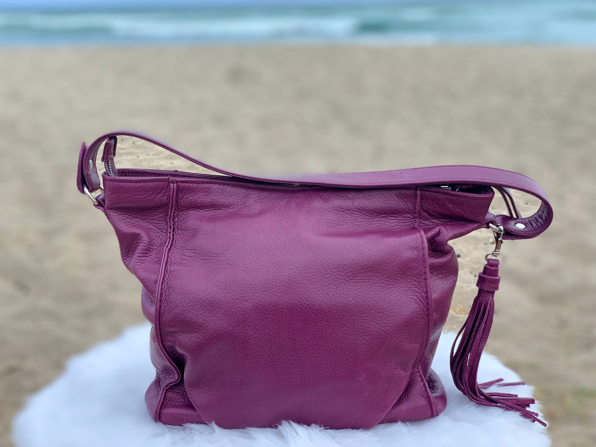 An aubergine hobo bag back view on a white surface with a beach background