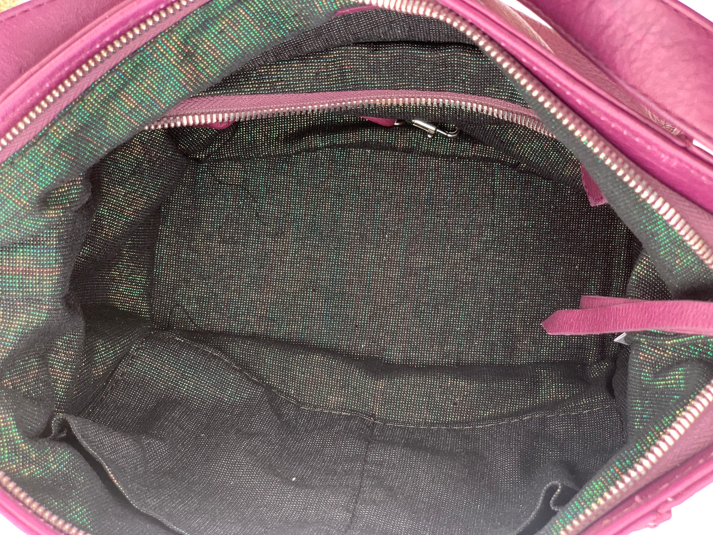 Close-up of the aubergine leather bag  interior with a visible brand logo on a black pearl iridescent textile lining, zip pocket, and two slip mobile pockets.