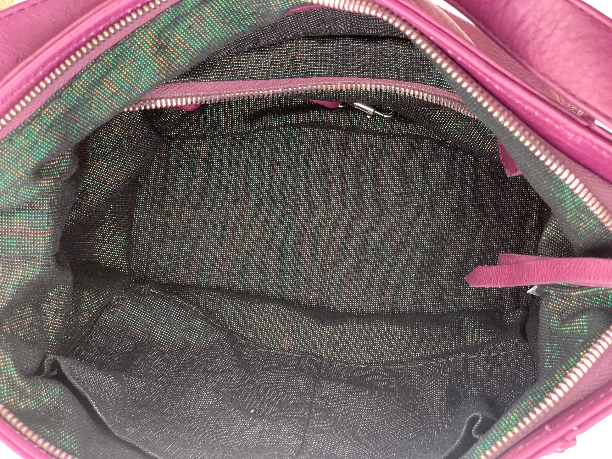 Close-up of the aubergine leather bag  interior with a visible brand logo on a black pearl iridescent textile lining, zip pocket, and two slip mobile pockets.