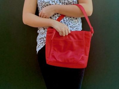 A woman holding a scarlet red bag in the crook of her arm against a dark background