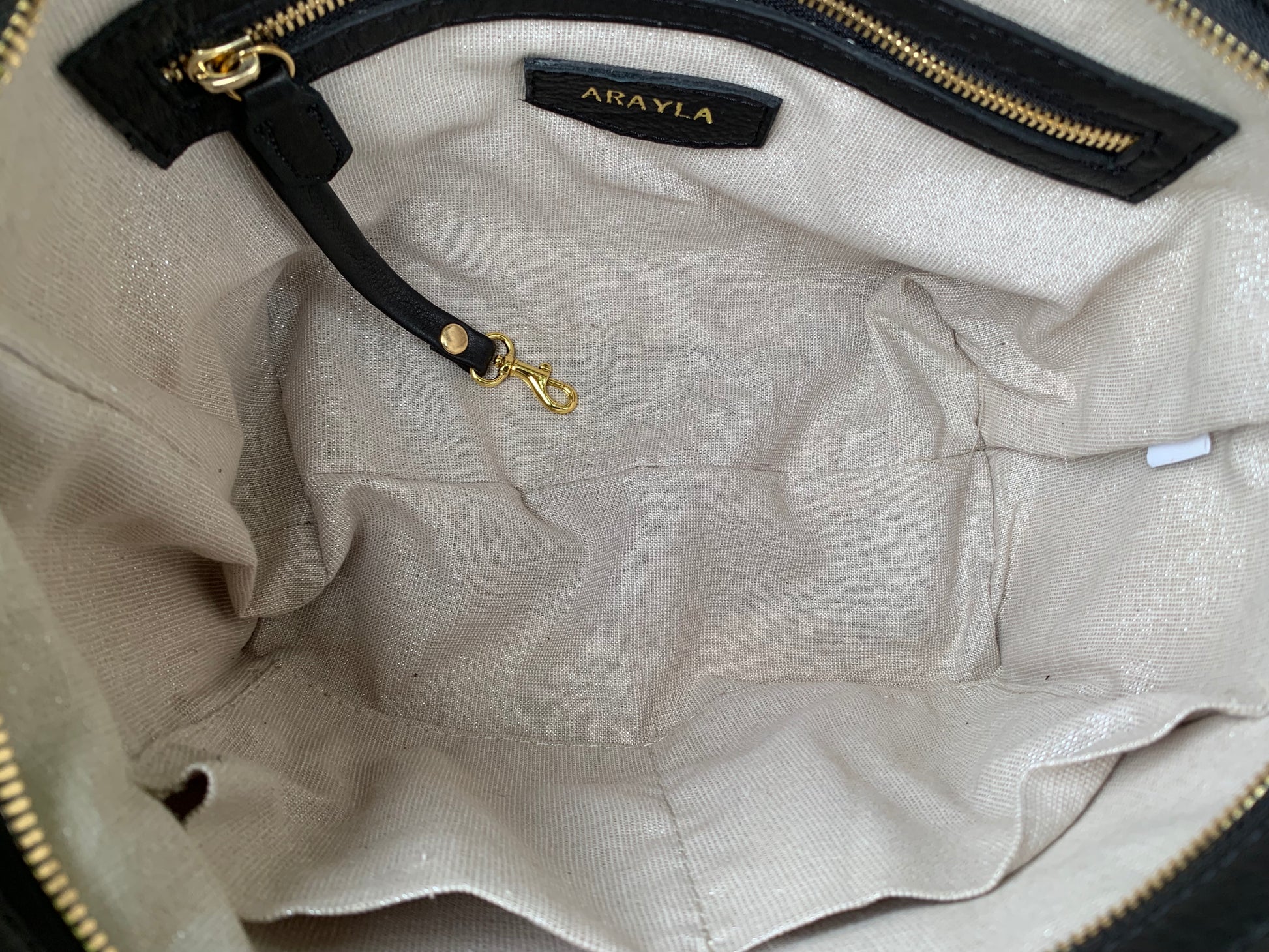 Close-up of the onyx black leather totebag  interior with a visible brand logo on a Silver sand textile lining, key leash, zip pocket, and two slip mobile pockets.