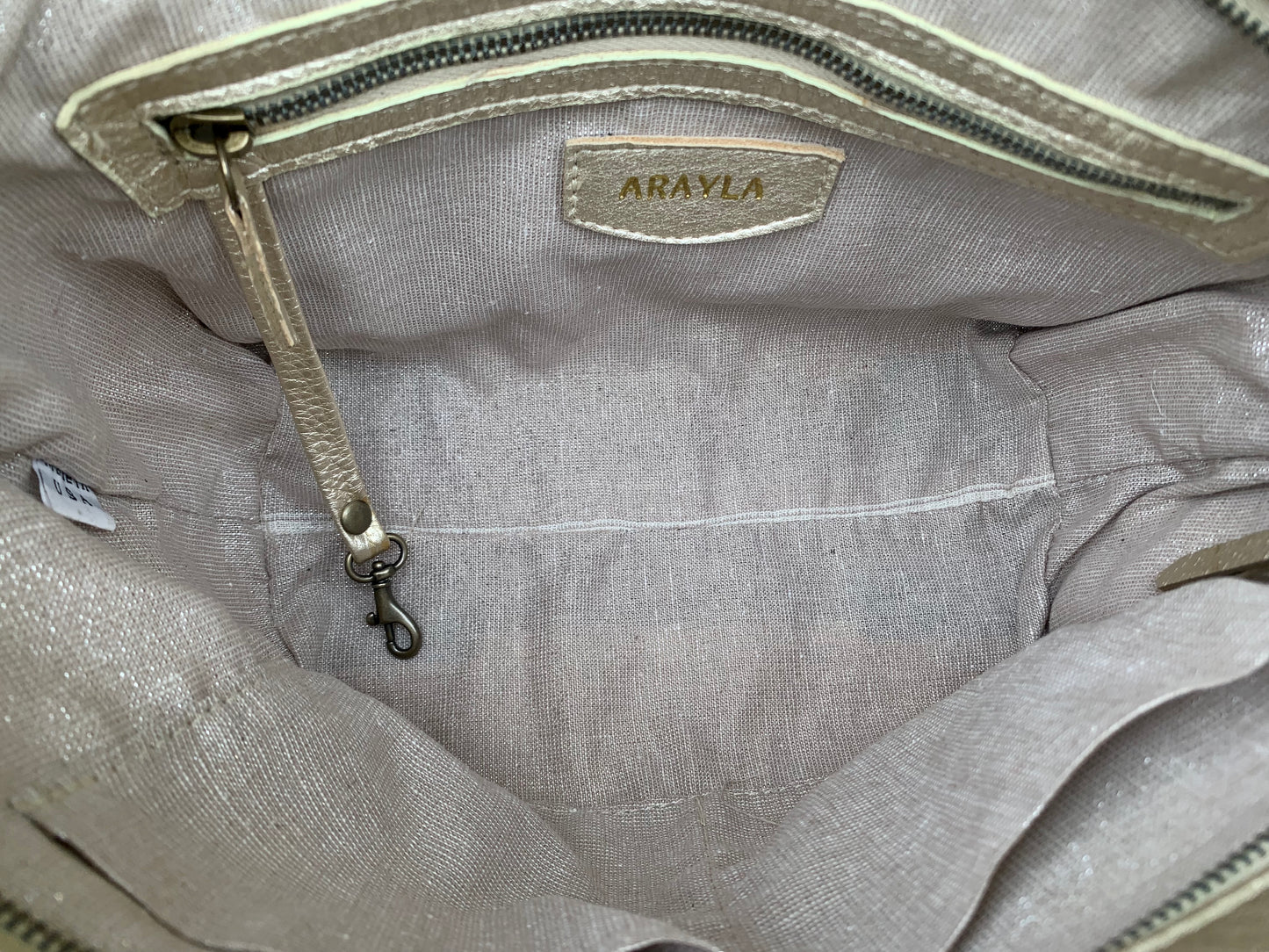 Close-up of the whisky brown leather bag  interior with a visible brand logo on a silver sand textile lining, key leash, zip pocket, and two slip mobile pockets.
