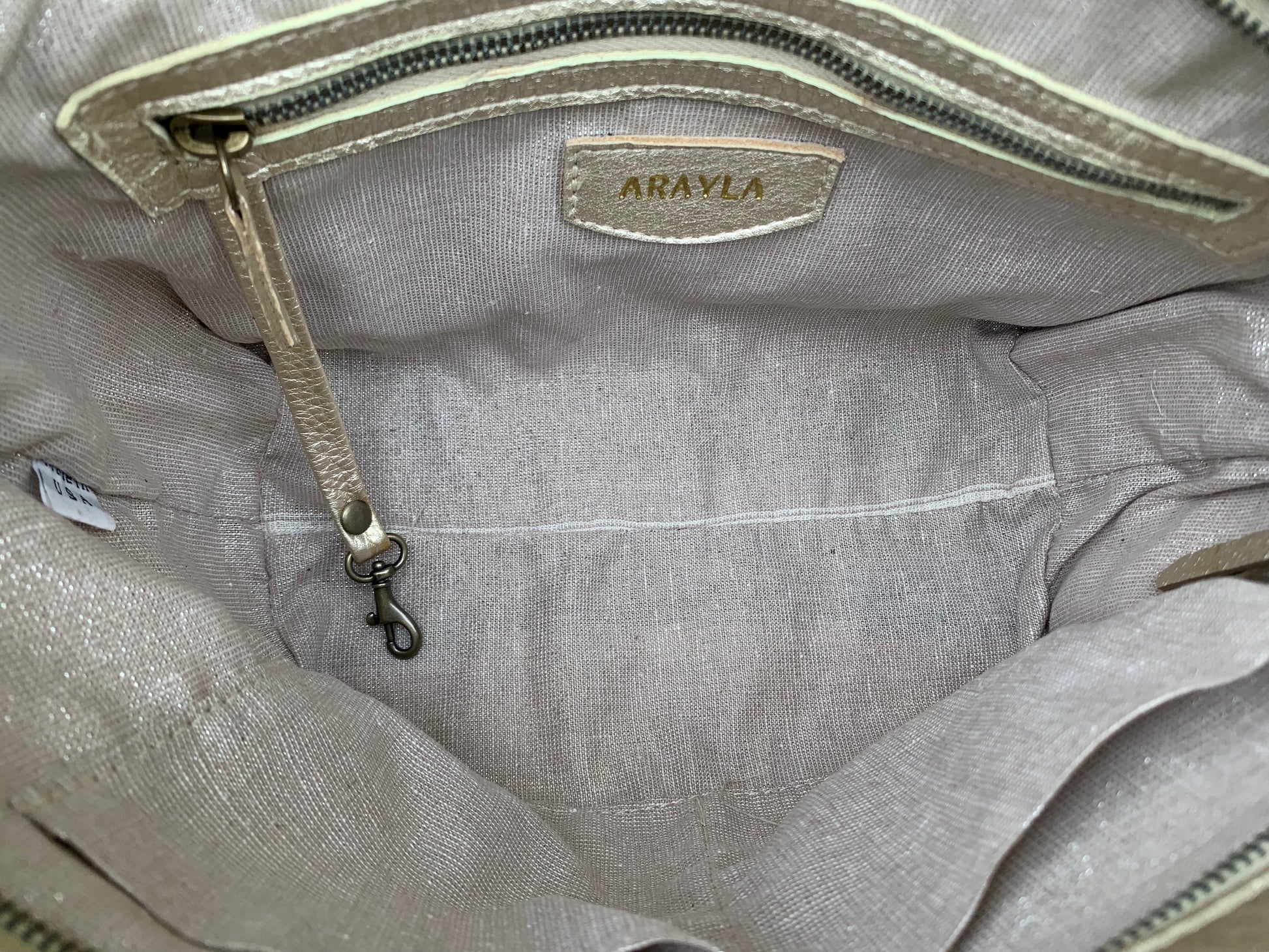 Close-up of the whisky brown leather bag  interior with a visible brand logo on a silver sand textile lining, key leash, zip pocket, and two slip mobile pockets.