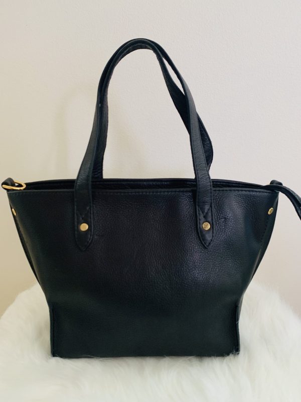 Onyx black leather tote bag back view with gold hardware on a white surface