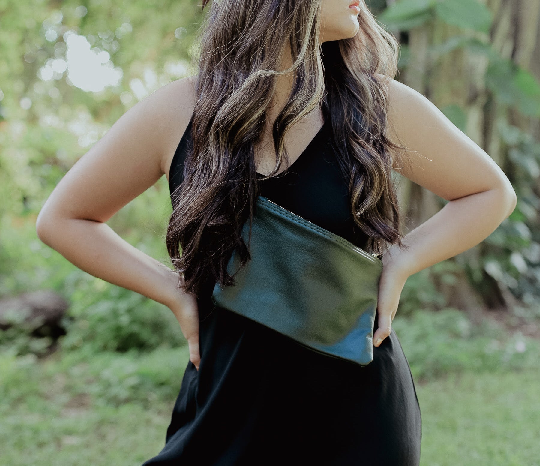 A woman wearing a across her chest over a black sleeveless dress, standing outdoors.
