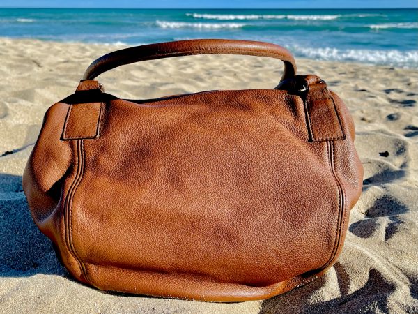 Brandy leather bag with slouchy structure on a sandy beach with ocean waves in the background