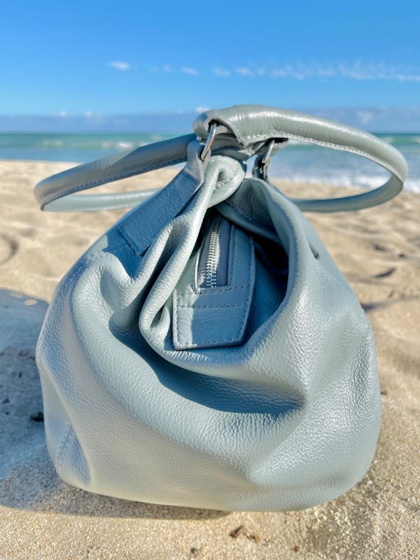 Light grey bag side veiw with a slouchy structure on a sandy beach with ocean view