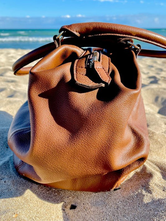Brandy leather bag side view with a slouchy structure on a sandy beach with an ocean view