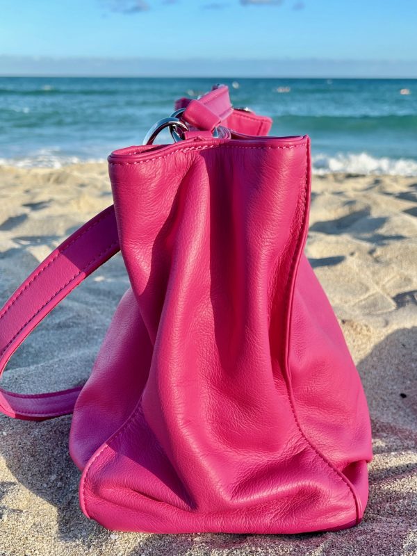 Hibiscus Pink bag side view with slouchy structure on a sandy beach with ocean in the background
