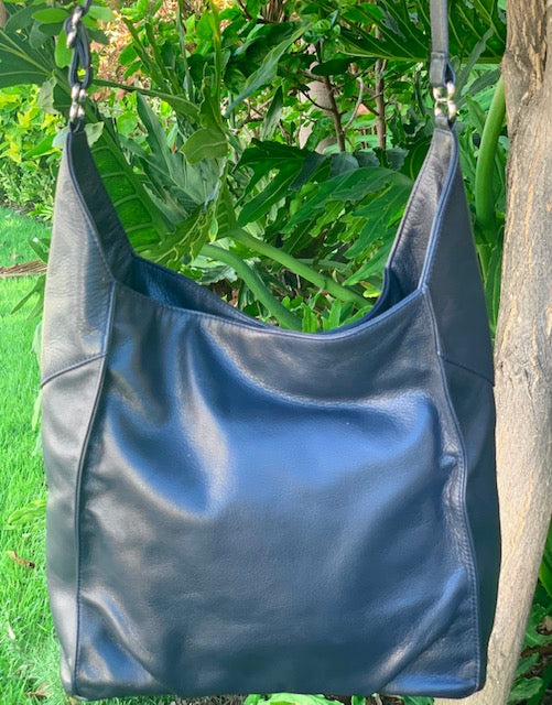 Sapphire leather hobo bag back view hanging on a tree branch with green leaves in the background