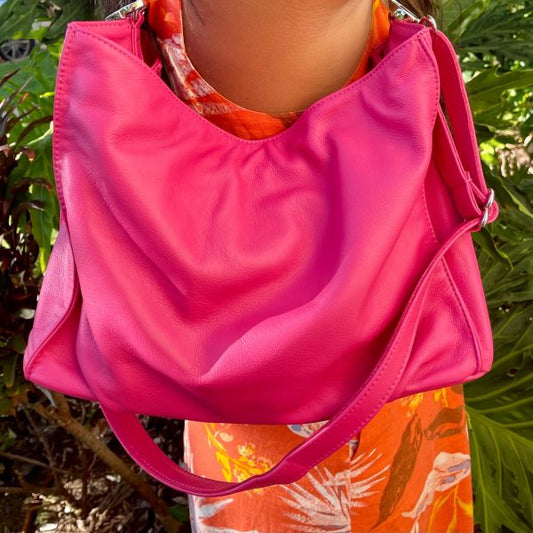A woman holding a bright hibiscus pink bag on her shoulder with a colorful garment in the background