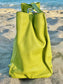 Tahitian lime leather bag side view on a sandy beach with ocean in the background