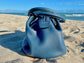Denim Blue leather bag side view on a sandy beach with ocean in the background