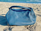 Denim Blue bag with slouchy structureon a sandy beach with ocean in the background