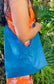 A woman wearing a floral orange dress holding a Cobalt Blue leather hobo bag as a crossbody bag.