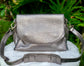 Pewter Metallic leather bag front view, on a white surface with green foliage in the background