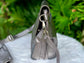 Pewter Metallic leather bag side view with long strap on a white surface with green leaves in the background