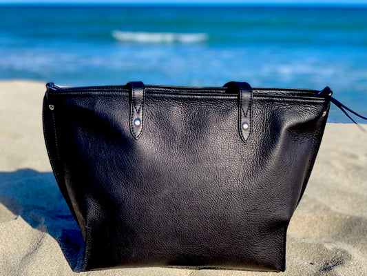  Onyx Black leather tote bag back vienw on a sandy beach with ocean in the background
