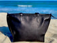  Onyx Black leather tote bag back vienw on a sandy beach with ocean in the background