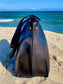 Onyx Black tote bag side view, on sand with ocean in the background.